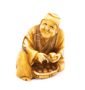 JAPAN 1910'S MEIJI PERIOD CARVED NETSUKE OF A SEATED MAN WITH BASKET