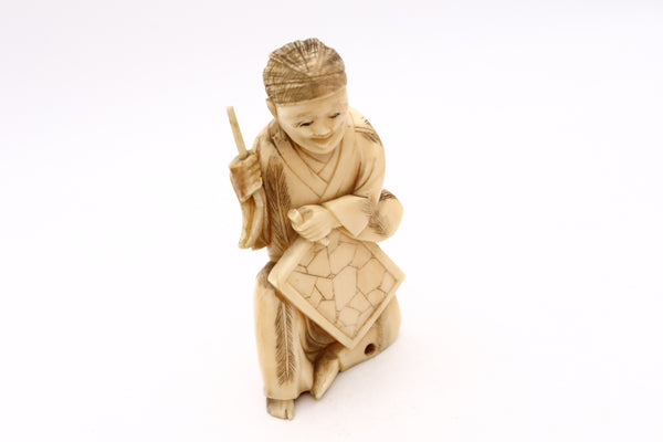 JAPAN 1900 MEIJI PERIOD CARVED NETSUKE OF A SEATED AND DRESSED STONE CARVER