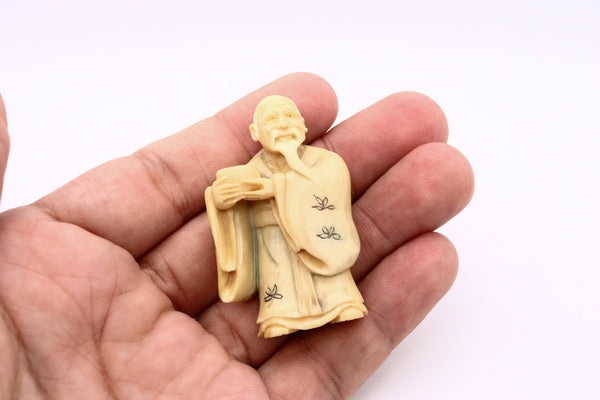 JAPAN 1900'S MEIJI PERIOD CARVED NETSUKE OF A STANDING OLD MAN WITH VESSEL